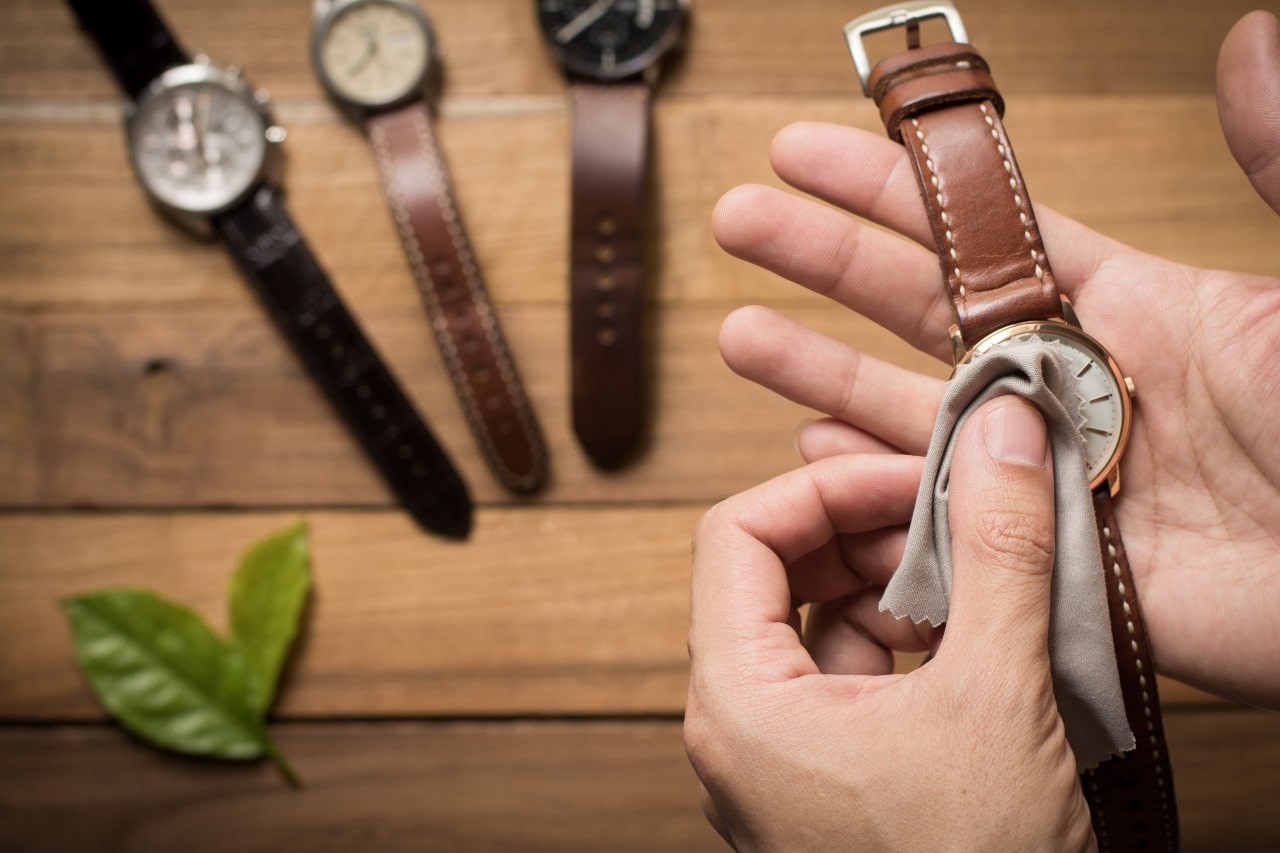 A close-up of a man polishing the crystal of a luxury watch, with 3 others resting atop a rustic wooden surface.