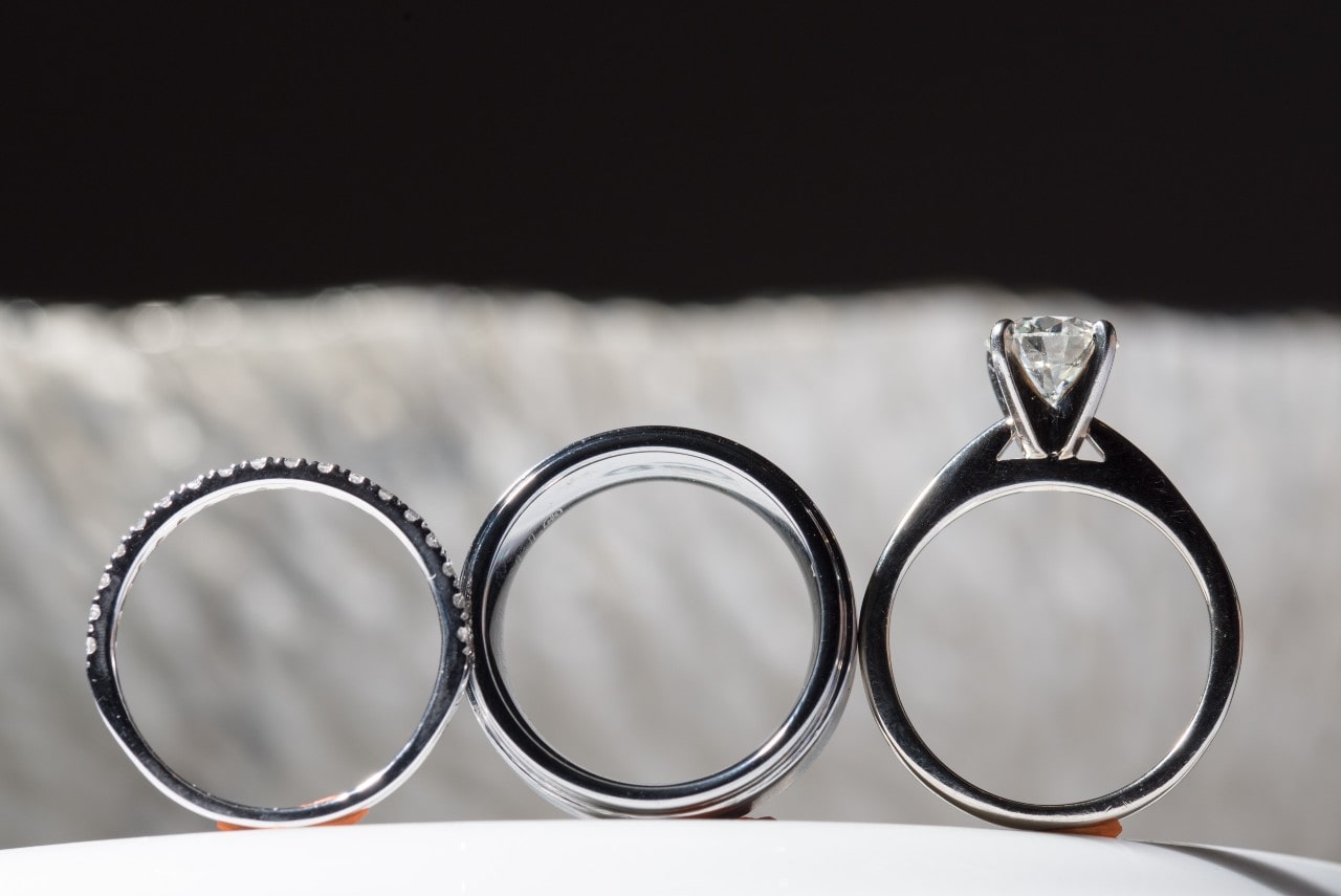A close-up of three rings— a side stone band, a minimalist band, and a solitaire engagement ring. A close-up of three rings— a side stone band, a minimalist band, and a solitaire engagement ring.