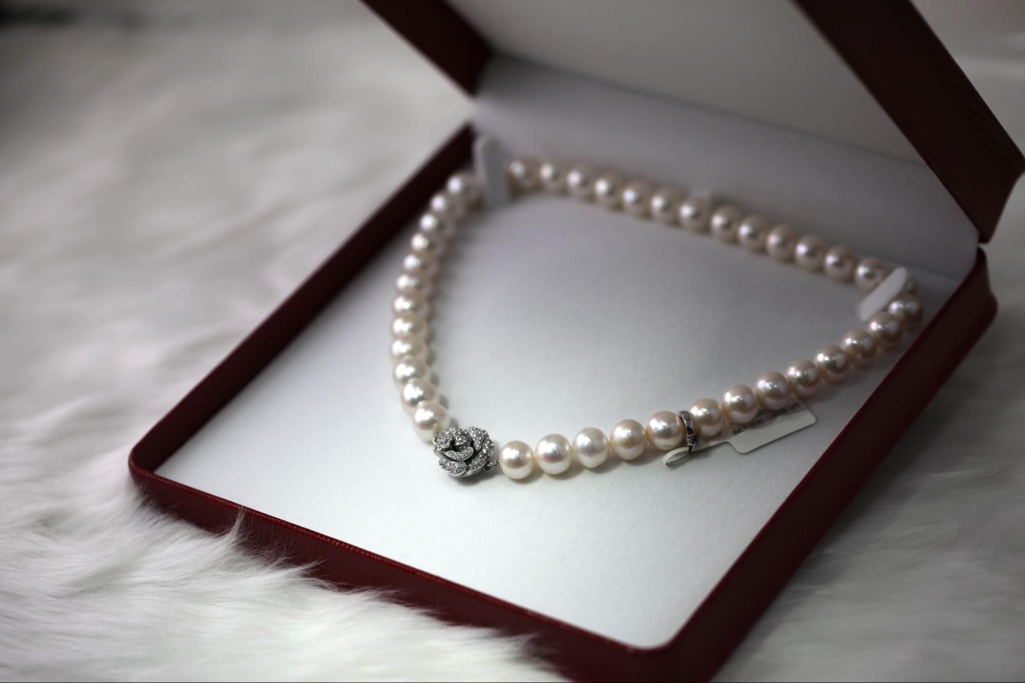 A close up of a pear necklace with diamond flower at the center inside the white and red jewelry box.