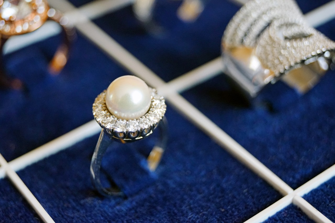 A close up of a diamond and pearl fashion ring on top of the deep blue velvet surface.