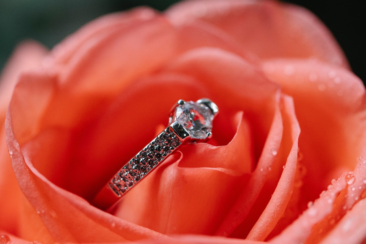 A round cut side stone ring in the center of an orange rose