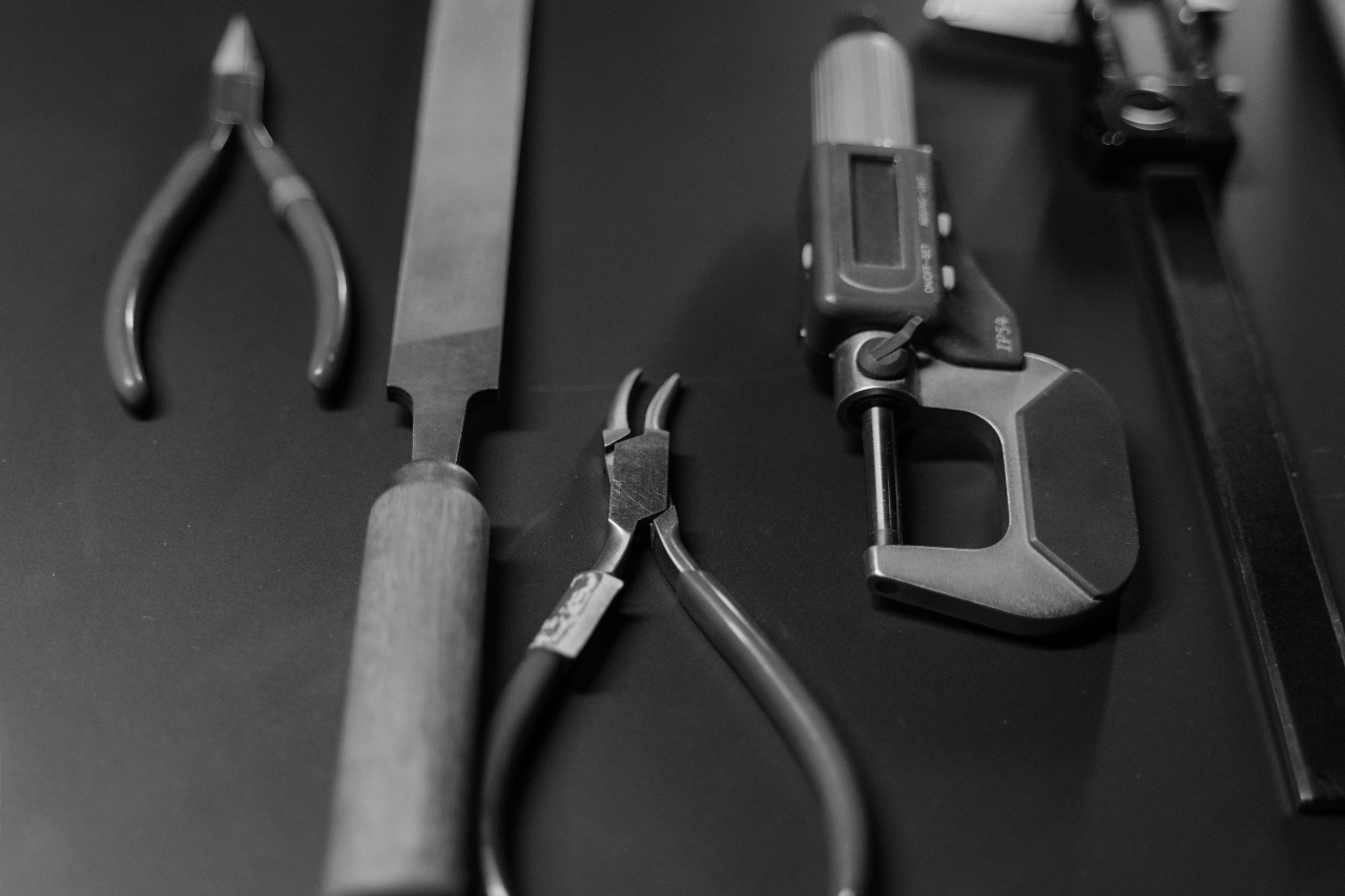 A black and white close-up of jeweler’s repair tools laid on a tabletop. A black and white close-up of jeweler’s repair tools laid on a tabletop.